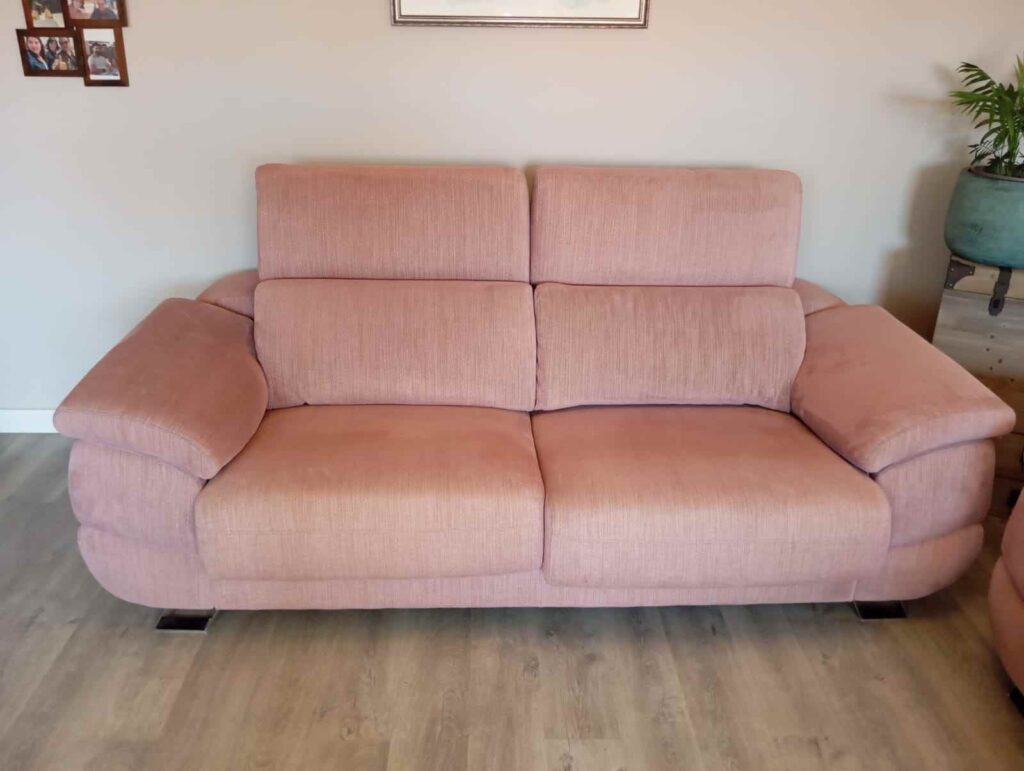 Sofá reclinable rosa en una sala de estar minimalista. Para mantener un sofá en buen estado, es importante realizar una limpieza superficial semanal, eliminando polvo y suciedad acumulada, y programar una limpieza profunda cada seis meses para alargar su vida útil y mantenerlo libre de bacterias y manchas